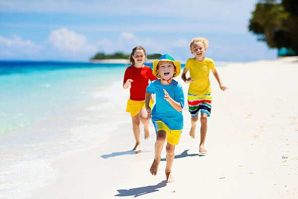 Kinder laufen am Strand mit Badeschutzkleidung